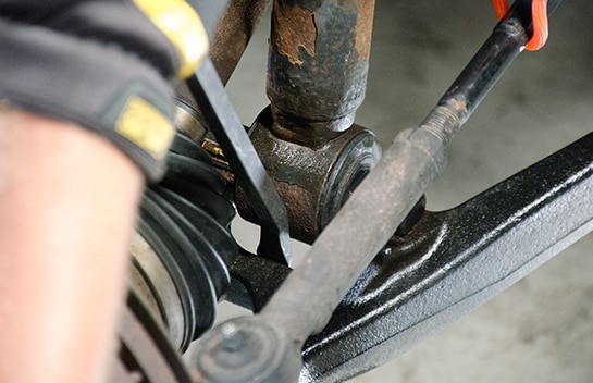 Mechanic using a pry bar to remove the bottom of the strut